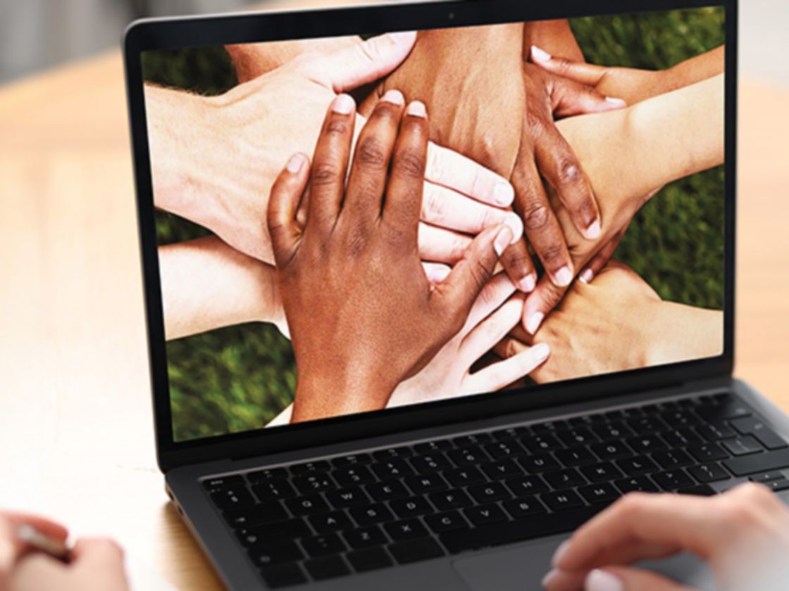 Un laptop aperto appoggiato su un tavolo, sullo schermo delle mani intrecciate di più persone.