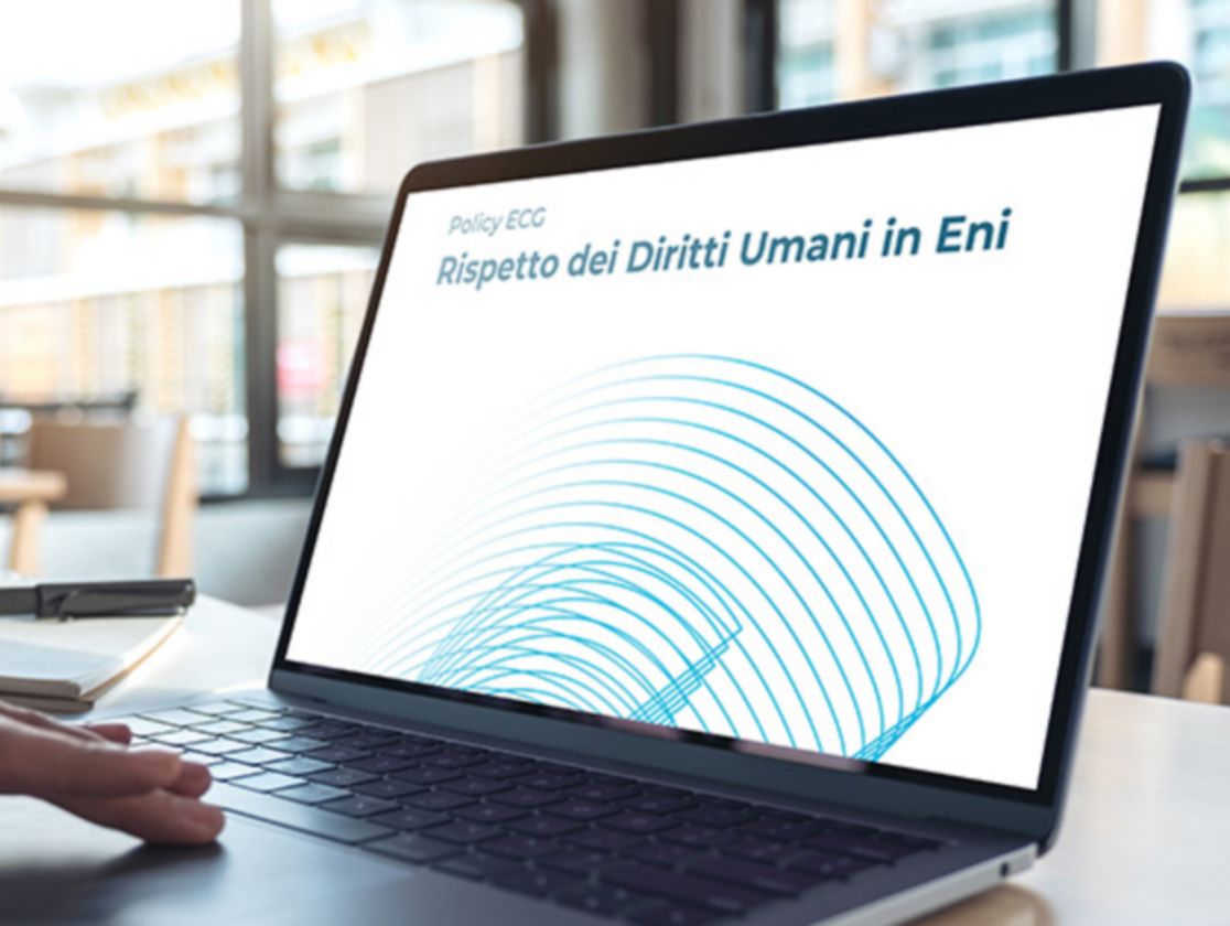  In a room, a hand moves across a laptop, and the screen reads: “ECG Policy, Respect for Human Rights at Eni” in Italian.