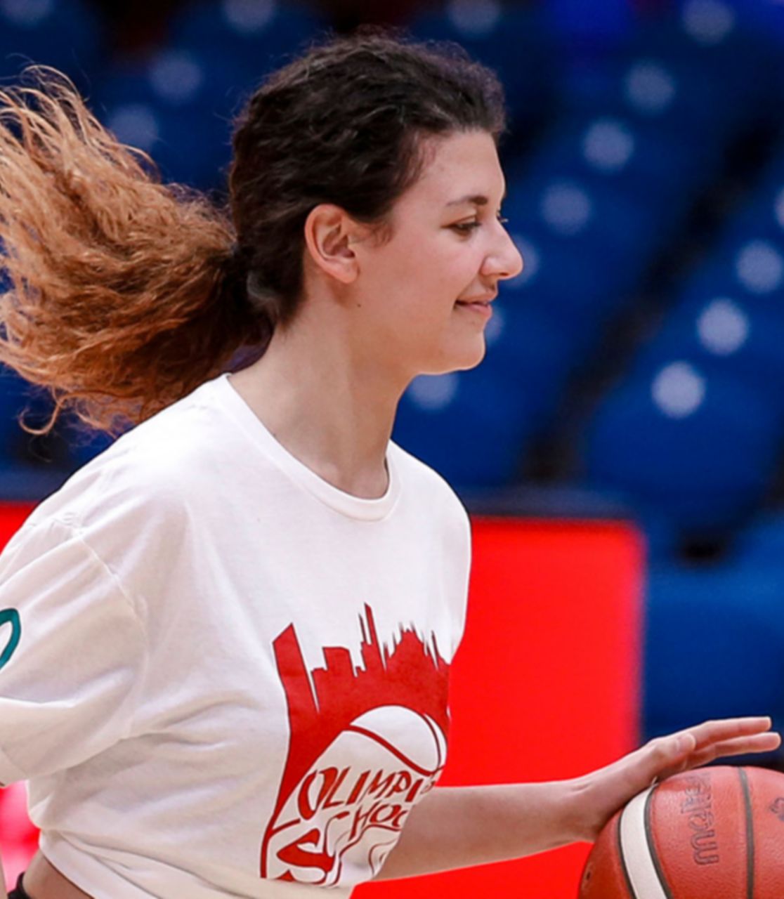 Una ragazza palleggia su un campo da basket vestita con una divisa di Olimpia Milano.