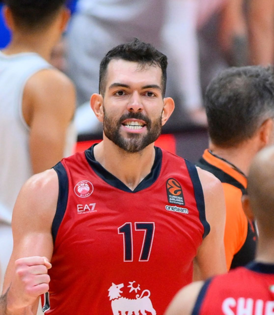 Due giocatori di basket con la maglia rossa con il logo Plenitude sono in primo piano di spalle, di fronte ad un terzo giocatore vestito uguale che li guarda stringendo un pugno in segno di vittoria. 