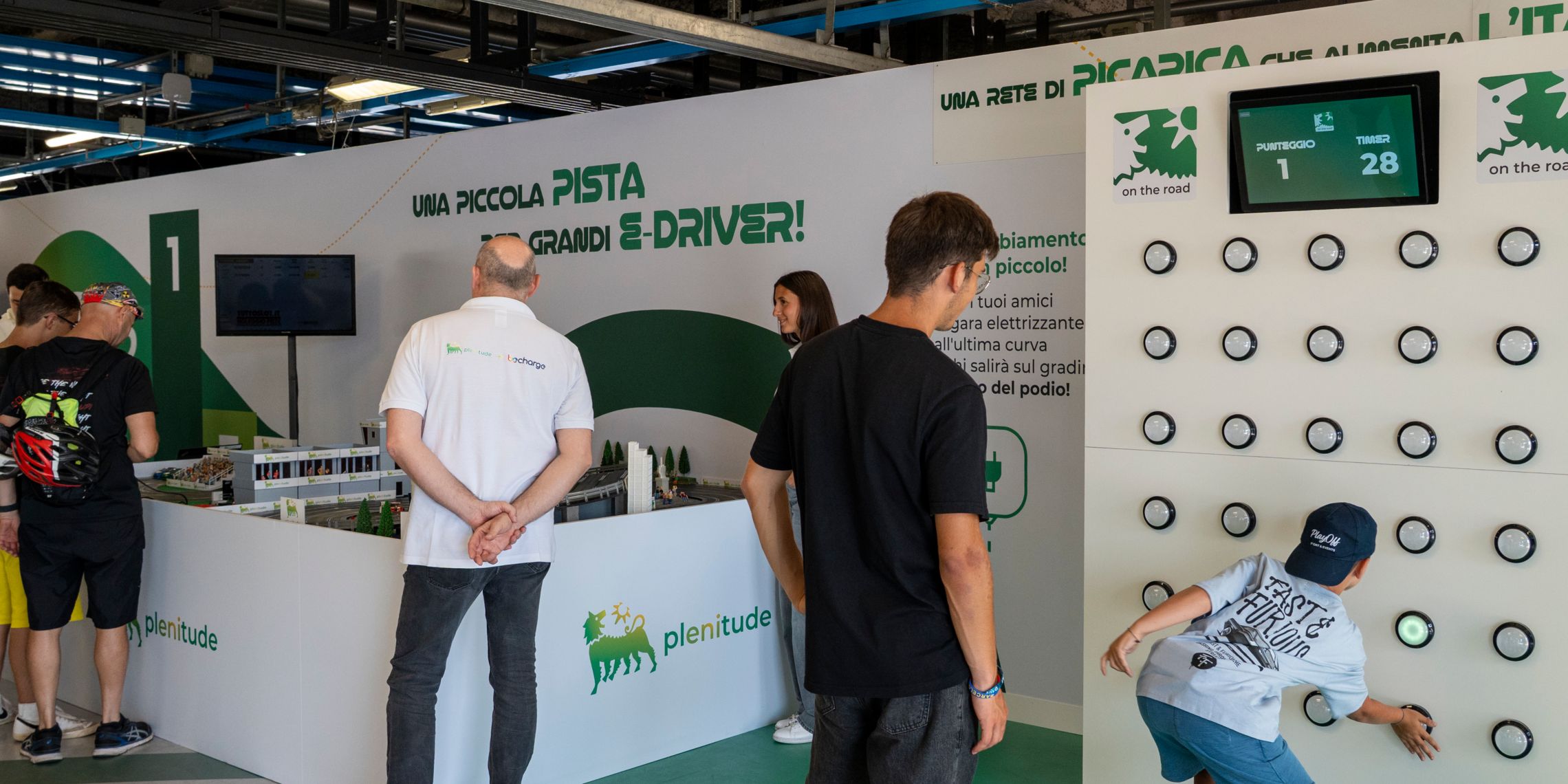 Two girls in a car look out the window at a woman near the electric car.