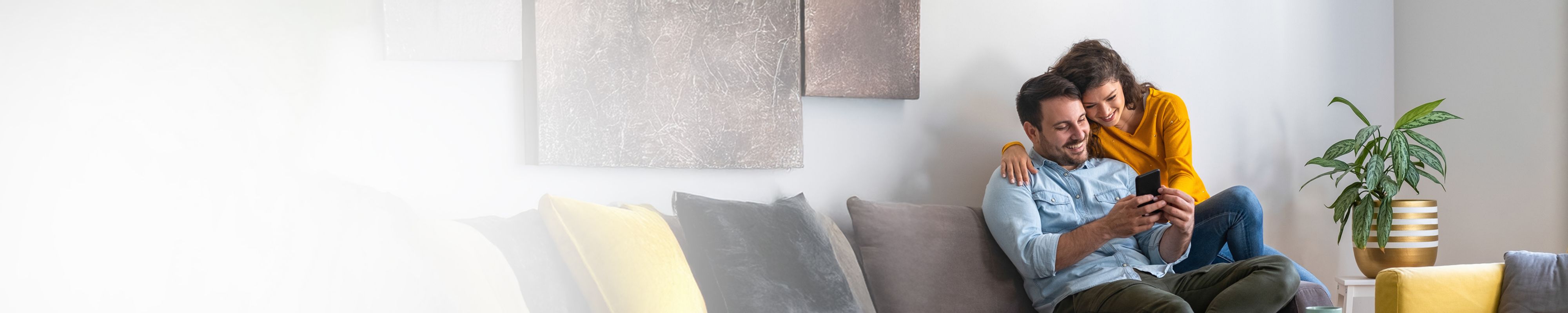 Fotografia de casal feliz e a sorrir, sentado no sofá a olhar para o telemóvel onde consultam o seu escalão de potência.