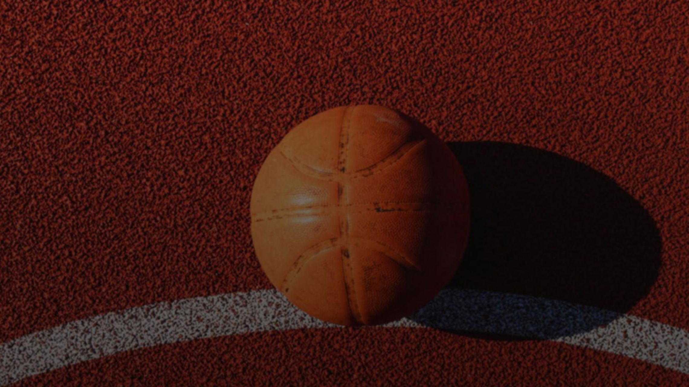 Campo da basket rosso con una riga bianca e una palla da basket appoggiata sul terreno che si vede in primo piano.