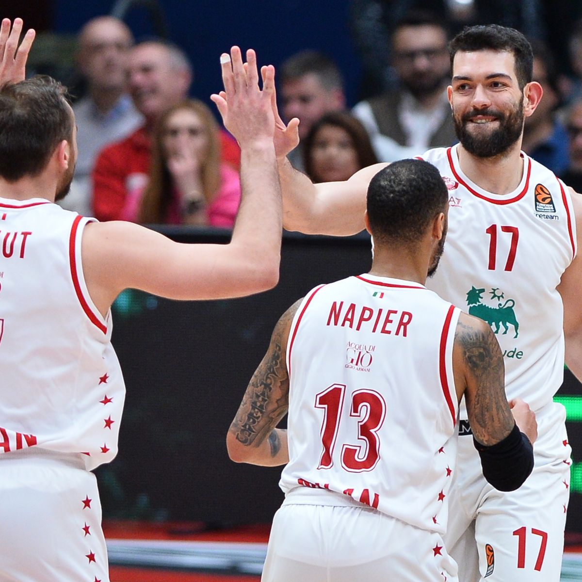 Tre giocatori di basket vestiti con una maglietta bianca, due di loro si danno il cinque.