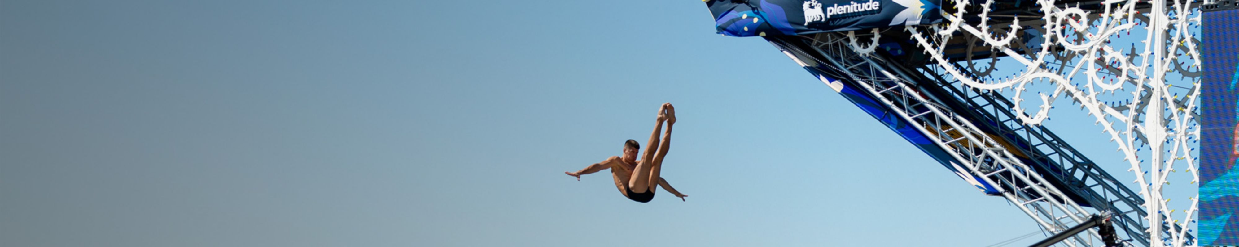 In a blue sky, a silhouette of a person attached to cables can be seen, appearing to fly through the air.