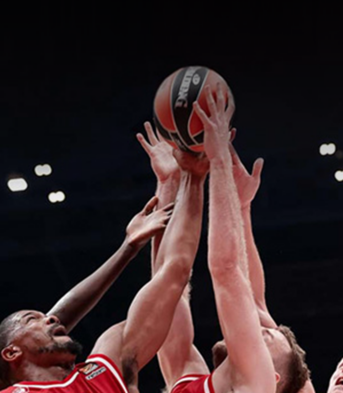 Giocatori vestiti con una maglietta rossa che cercano di prendere la palla da basket con un braccio.