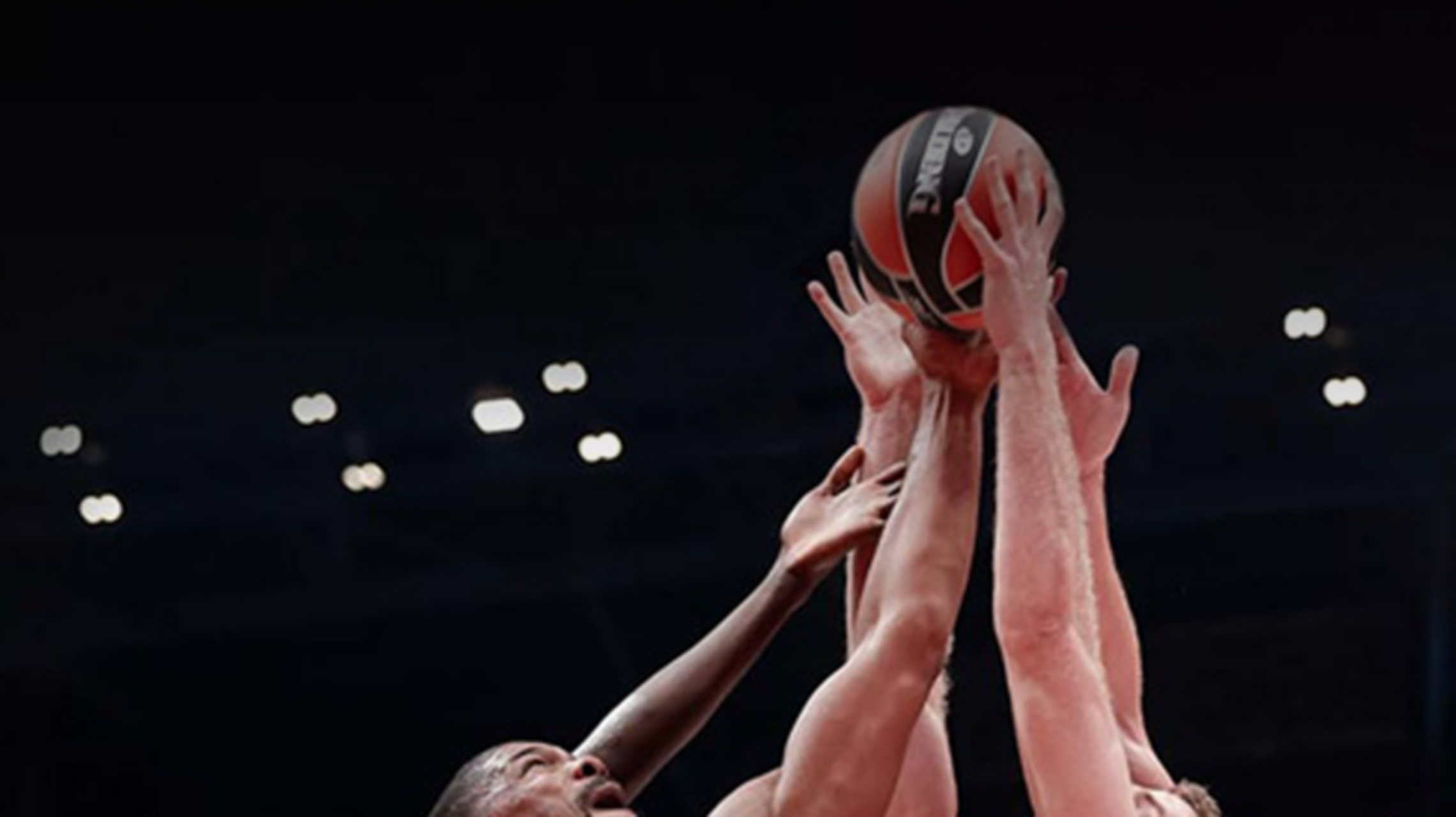 Players dressed in a red t-shirt, trying to catch the basketball with one arm.
