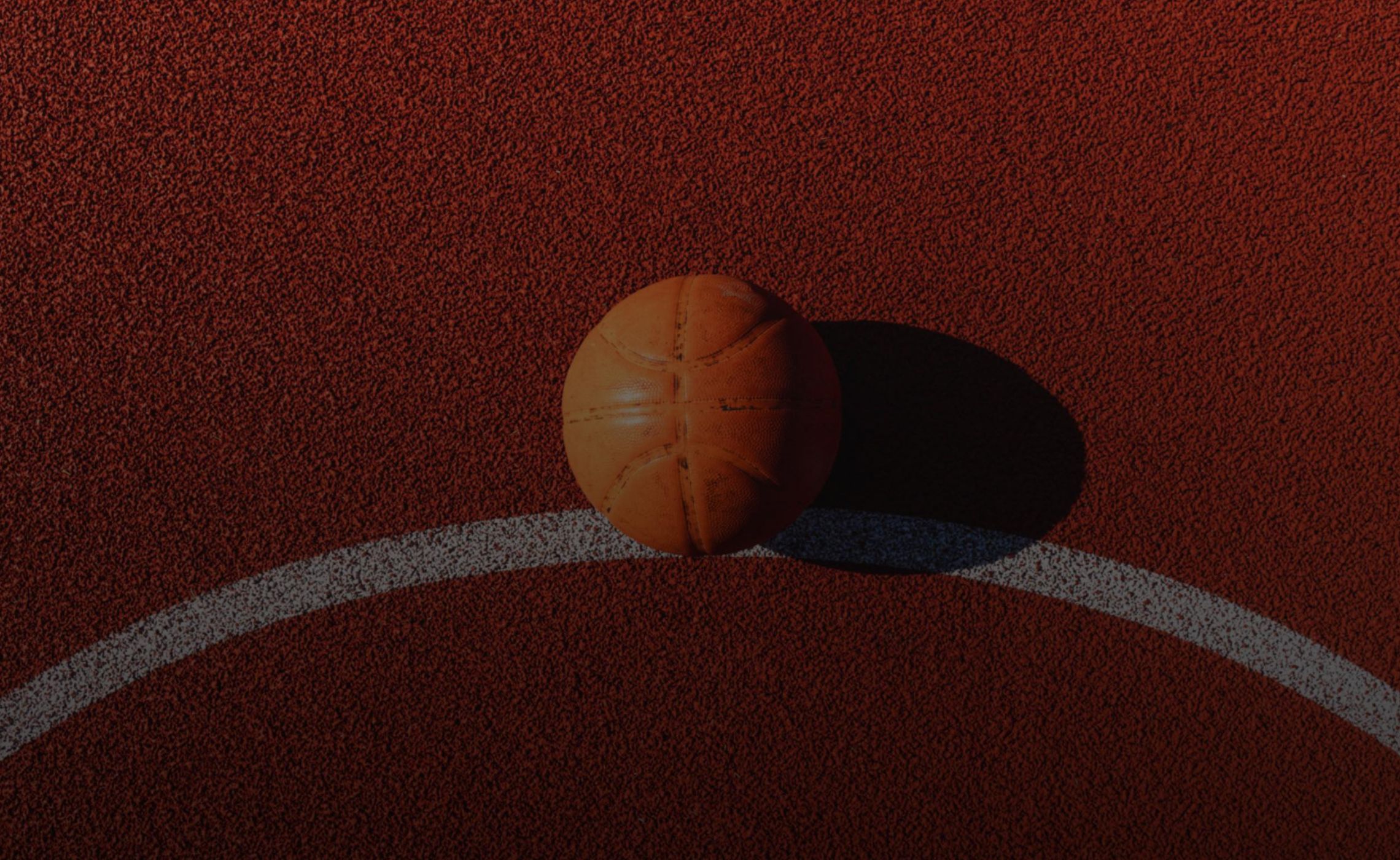Campo da basket rosso con una riga bianca e una palla da basket appoggiata sul terreno che si vede in primo piano.