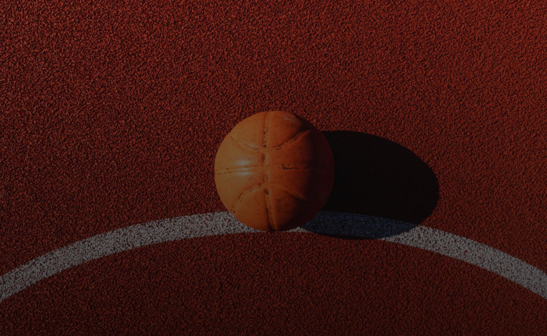 A top-down shot of an orange basketball resting on the ground on a red basketball court.