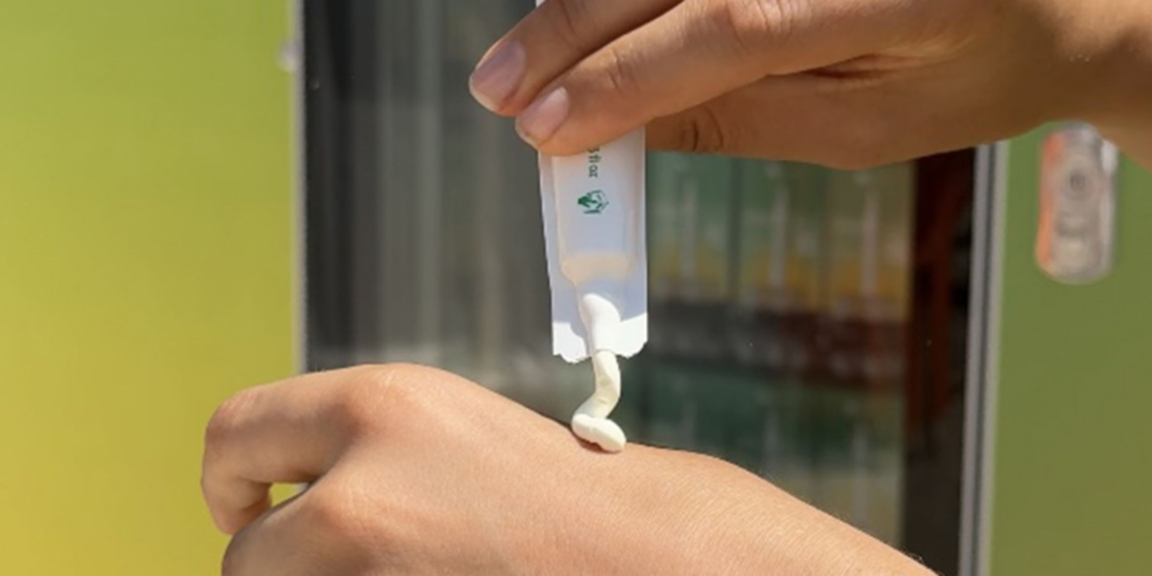 In primo piano c'è una mano che spreme su un'altra mano la crema solare di Plenitude. Sullo sfondo c'è il distributore di crema.