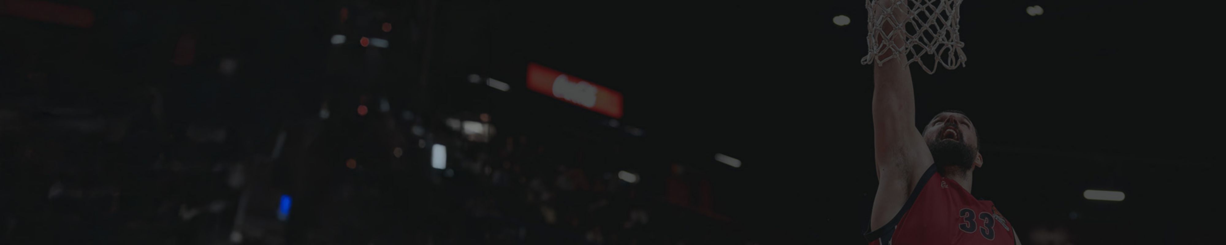 Si vede il volto di un giocatore con la barba e i capelli neri, vestito con una canottiera rossa da basket, che segna un canestro con il braccio destro teso verso l'alto.