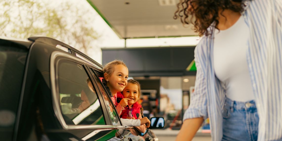 Due bambine in auto guardano dal finestrino una donna vicino alla macchina elettrica.